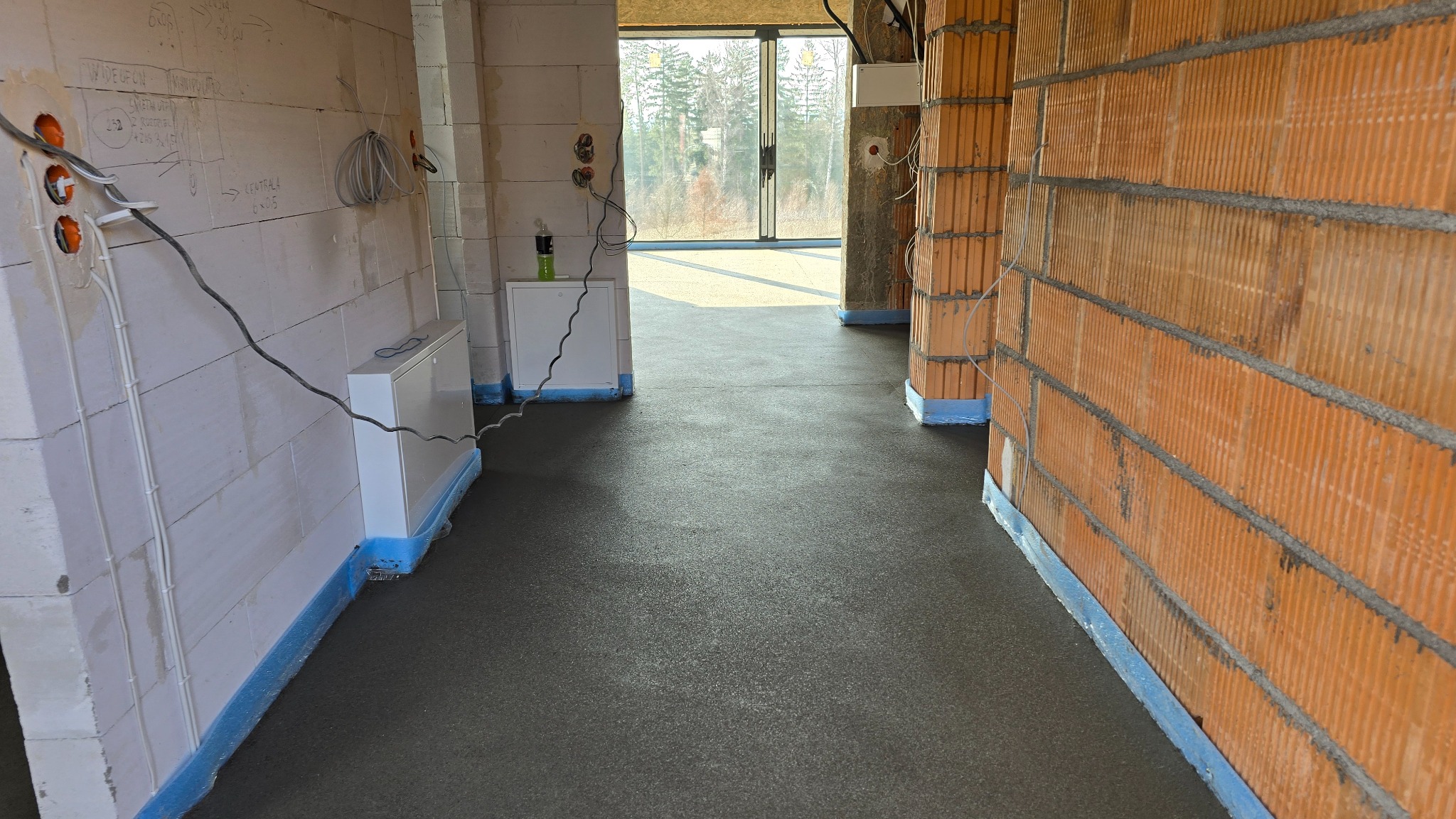 Świeża, gładka wylewka w surowym wnętrzu budynku w Stronie Śląskie. Widoczne ściany z pustaków i instalacje elektryczne. Ochrona przeciwwilgociowa przy ścianach.