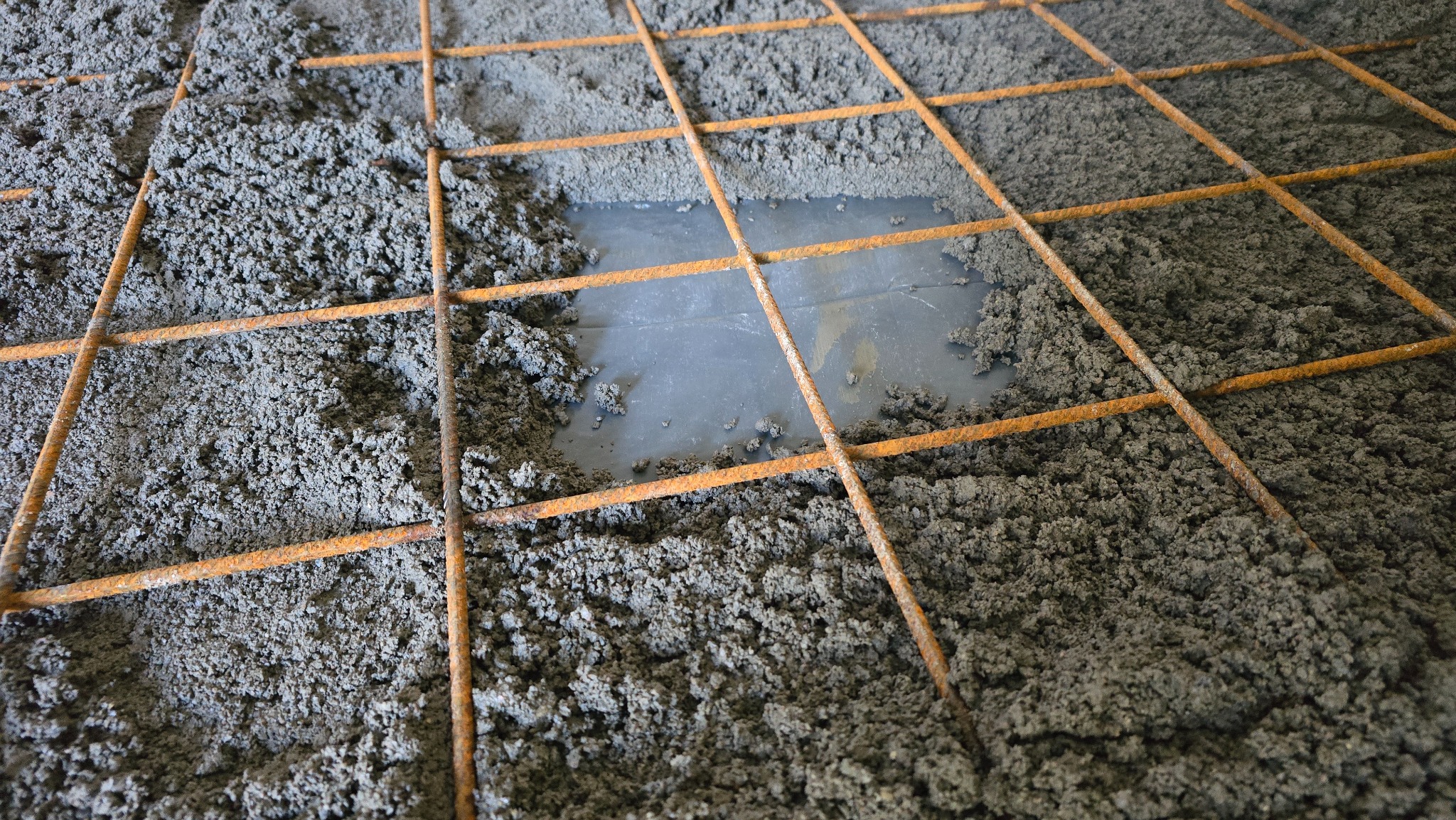 Wylewka jastrychowa zbrojona siatką stalową, częściowo pokryta folią. Widoczne nierównomierne rozprowadzenie masy jastrychowej. Detal z budowy posadzki.