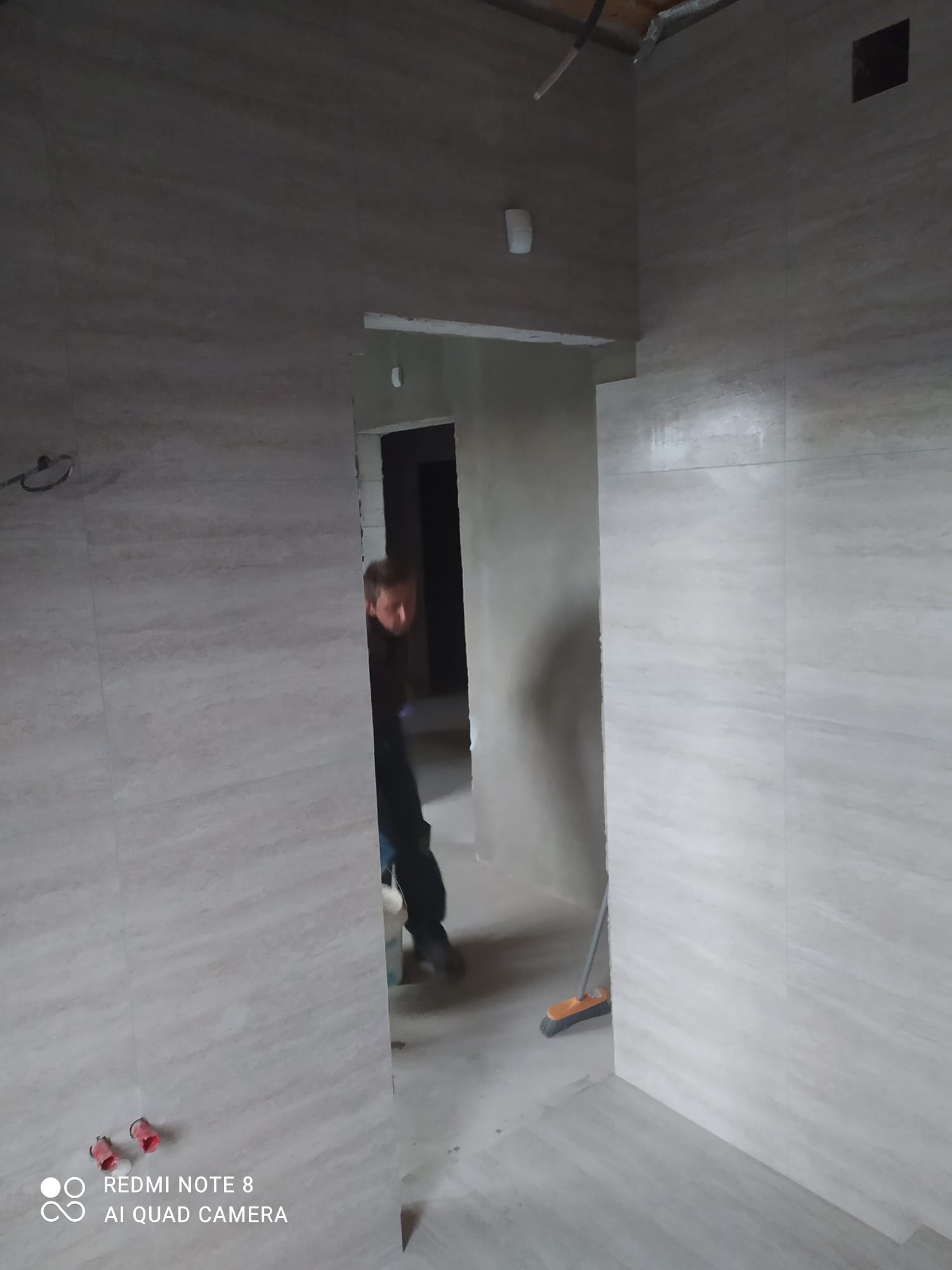 Układanie płytek imitujących drewno na ścianach łazienki, widoczny fragment osoby pracującej oraz akcesoria hydrauliczne na podłodze.