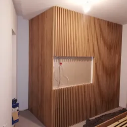 Montaż drewnianej ścianki działowej z listew z otworem na telewizor, widoczne przewody, surowy stan wykończenia wnętrza.