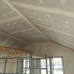 Sufit poddasza z płyt kartonowo-gipsowych w trakcie montażu, widoczne łączenia wzmocnione taśmą i szpachlą, na pierwszym planie rusztowanie.