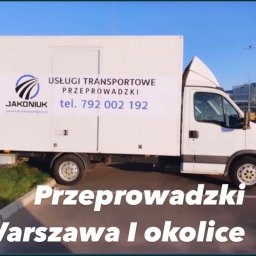 Transport przeprowadzki - Biała furgonetka z reklamą usług transportowych i przeprowadzkowych firmy Jakoniuk, zaparkowana na parkingu z budynkiem biurowym w tle.