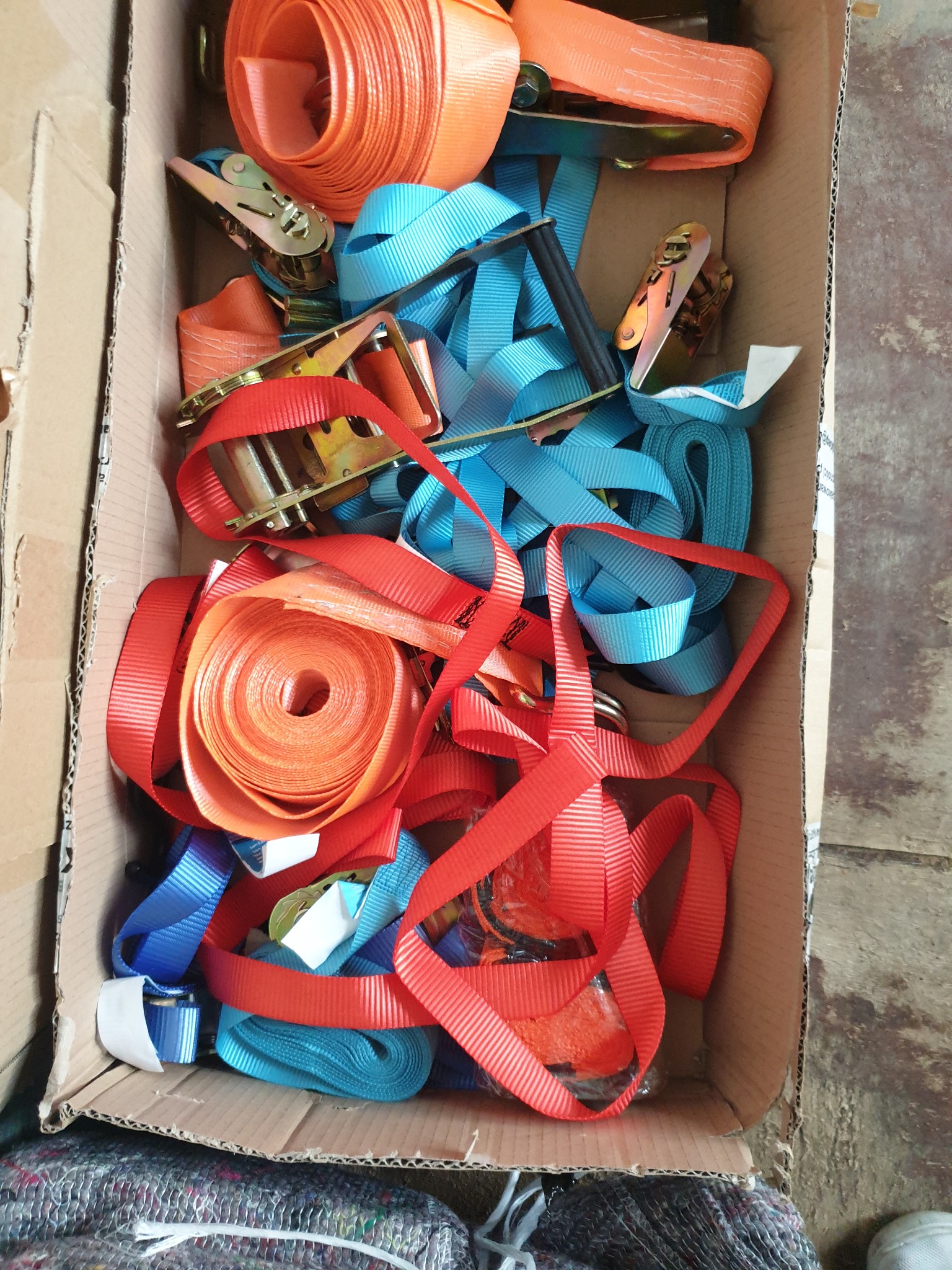 Pudełko kartonowe wypełnione zwiniętymi pasami transportowymi w kolorach: pomarańczowym, czerwonym i niebieskim, z metalowymi napinaczami.