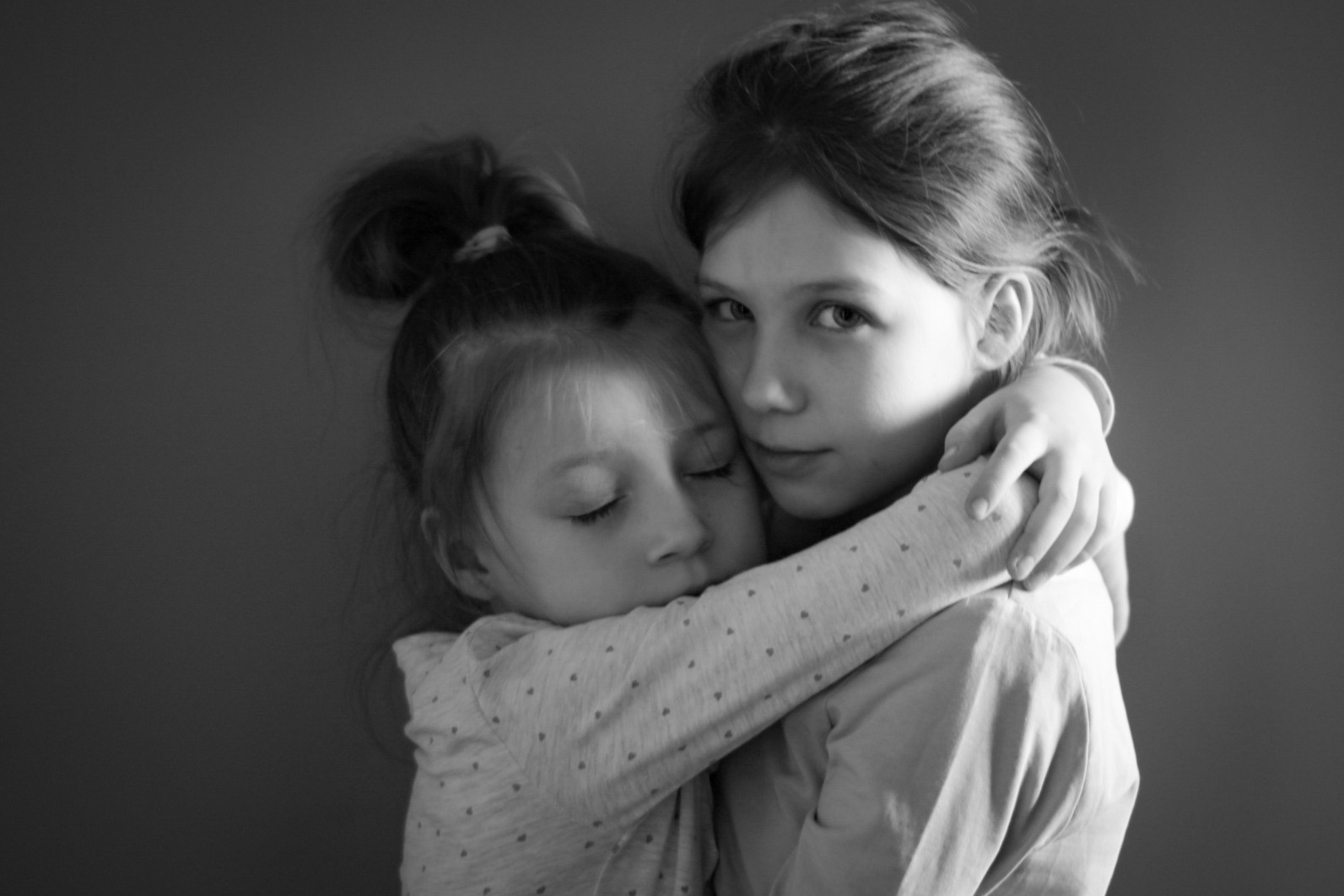 Portret czarno-biały dwóch sióstr, starsza obejmuje młodszą, która ma zamknięte oczy i opiera się o ramię starszej.