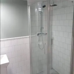 Nowoczesna kabina prysznicowa z deszczownicą i baterią termostatyczną, wykończona białymi, prostokątnymi płytkami, z szarą ścianą w tle i marmurową posadzką.