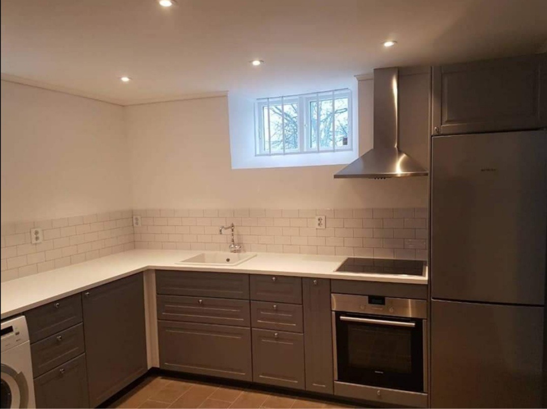 Szara kuchnia z białymi płytkami metra, narożnym blatem, srebrnym okapem i oknem z widokiem na drzewa.