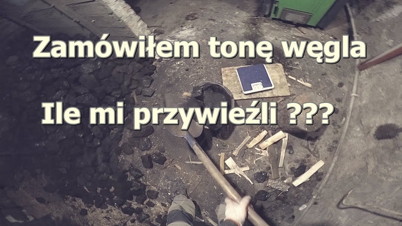 Kopalnia węgla: Łopata wbita w pryzmę czarnego paliwa, obok stoi waga elektroniczna na drewnianej desce, sugerująca kontrolę ilości dostarczonego materiału. W tle widoczny piec.