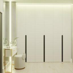 DACH.INTERIOR_DESIGN - Minimalistyczna garderoba z białymi frontami i długimi, czarnymi uchwytami, uzupełniona toaletką z lustrem i okrągłym pufem w jasnych barwach, oświetlona listwą LED.
