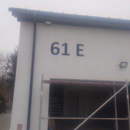 BUD-MAD ELEWACJE Sp. z o.o. - Biała elewacja budynku z numerem 61E, widoczne rusztowanie przed garażem, drzewa w tle, pochmurna pogoda.