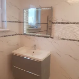 Nowoczesna łazienka z umywalką w szafce z szufladami, lustrem z podświetleniem LED i marmurowymi płytkami z dekoracyjnym pasem mozaiki.