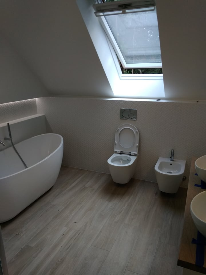 Nowoczesna łazienka na poddaszu w Kielcach z wolnostojącą białą wanną, toaletą, bidetem i drewnopodobną podłogą, oświetlona przez okno dachowe.