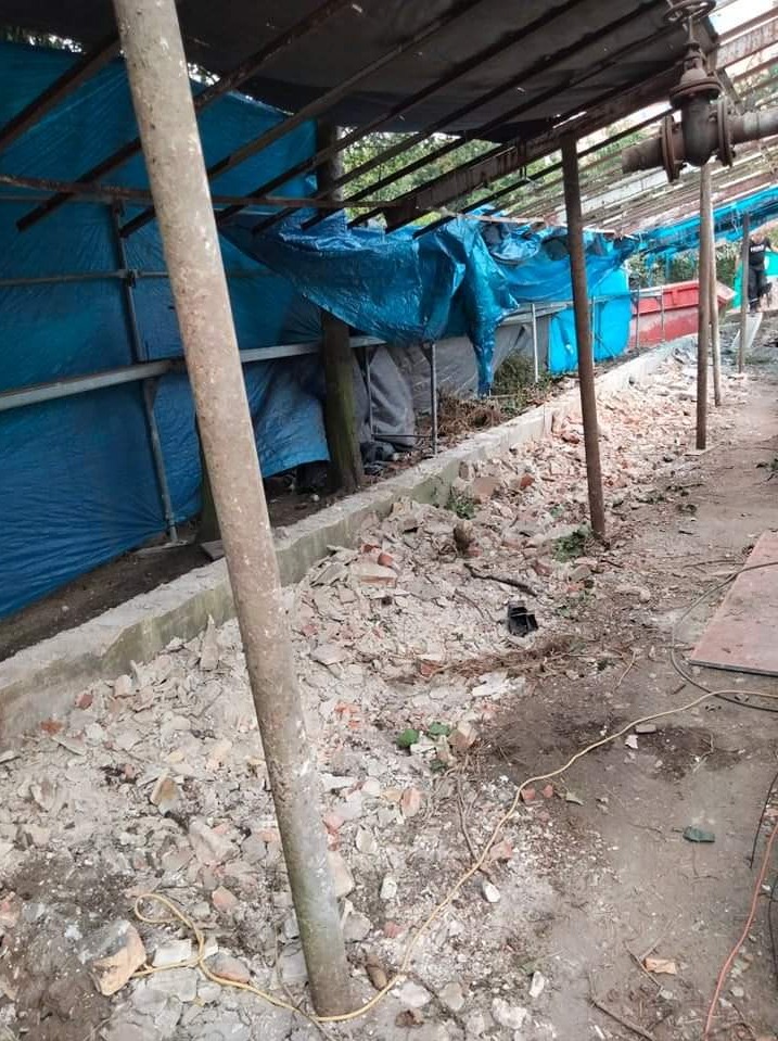 Teren po rozbiórce z fragmentami gruzu i cegieł, zabezpieczony niebieską plandeką, widoczne metalowe podpory i fragment instalacji przemysłowej.