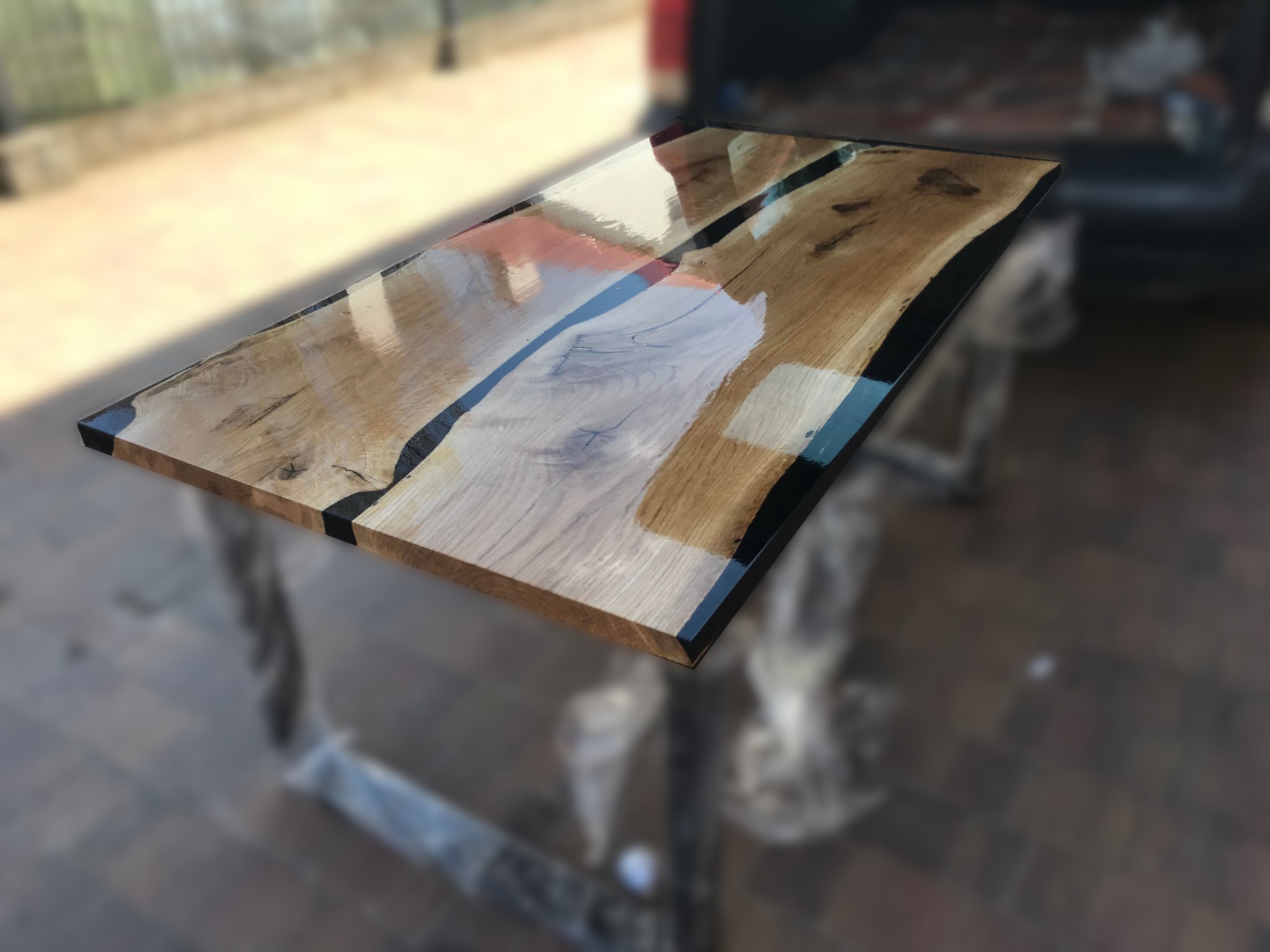 Stół z blatem z naturalnego drewna z żywicą epoksydową w kolorze niebieskim i czarnym, widoczne słoje drewna i nieregularne krawędzie, nogi stołu owinięte folią ochronną.