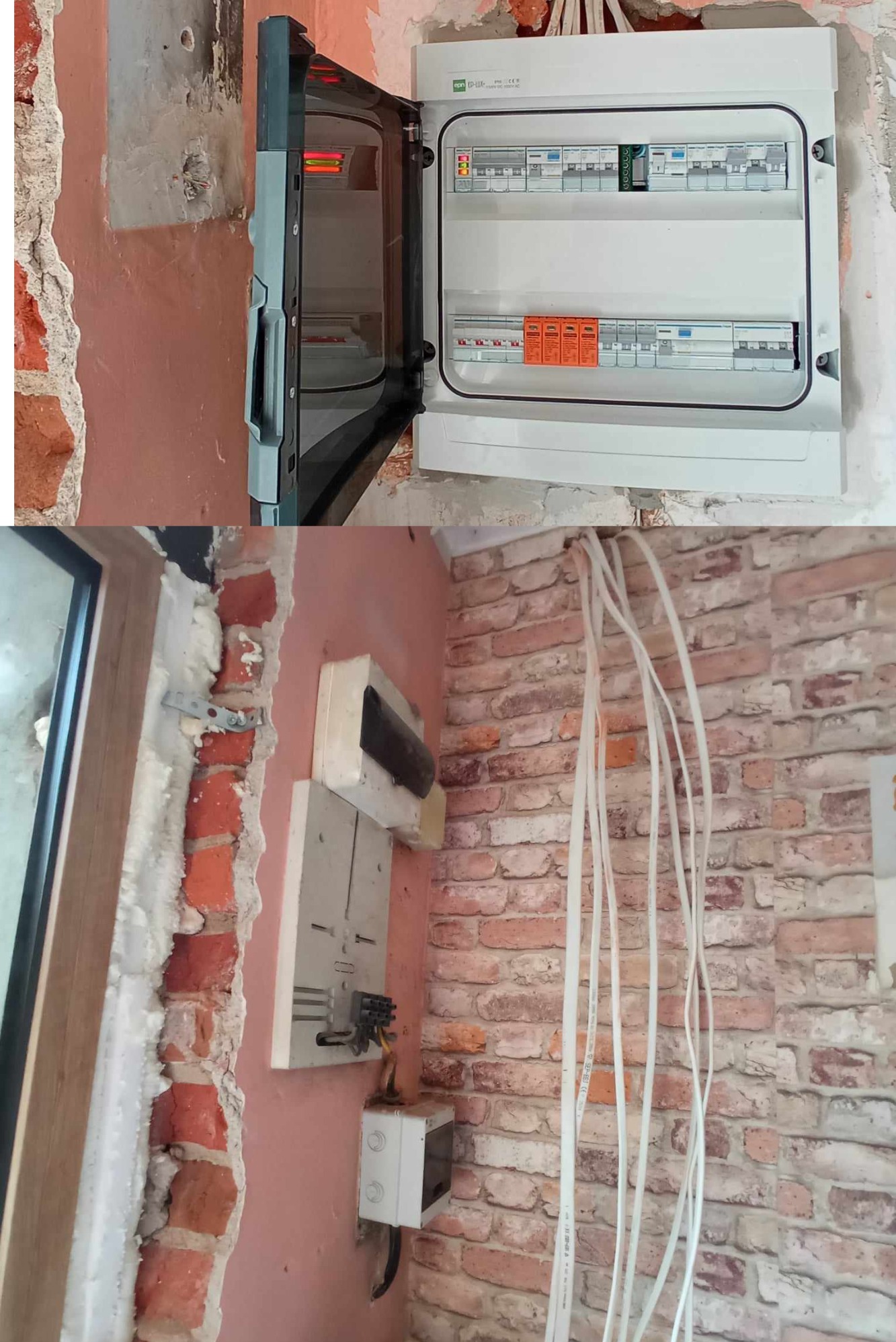 Otwarta rozdzielnica elektryczna z widocznymi bezpiecznikami i przewodami. W tle ściana z cegieł pokryta różową farbą. Widoczne kable wystające ze ściany, prowadzące do rozdzielnicy.