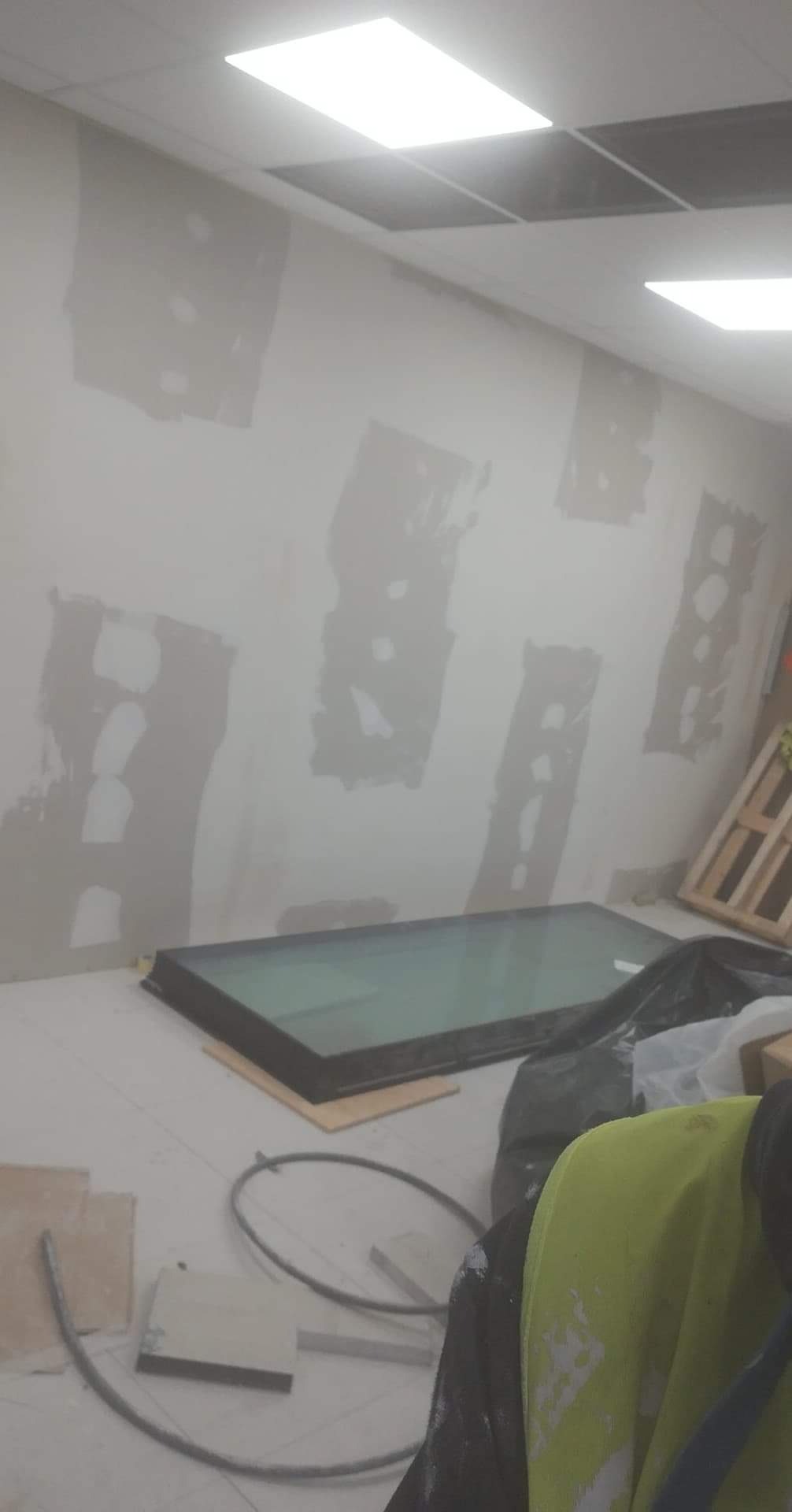 Przygotowanie ściany do dalszych prac wykończeniowych: widoczne fragmenty nałożonej gładzi, okno połaciowe leżące na podłodze, fragment roboczego ubrania z farbą.