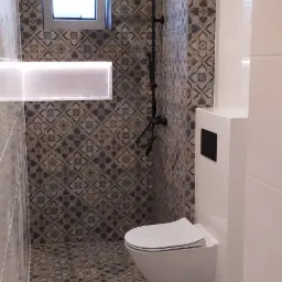 Nowoczesna łazienka z wiszącą toaletą, czarną armaturą prysznicową i dekoracyjną płytką podłogową oraz ścienną z motywem kwiatowym.