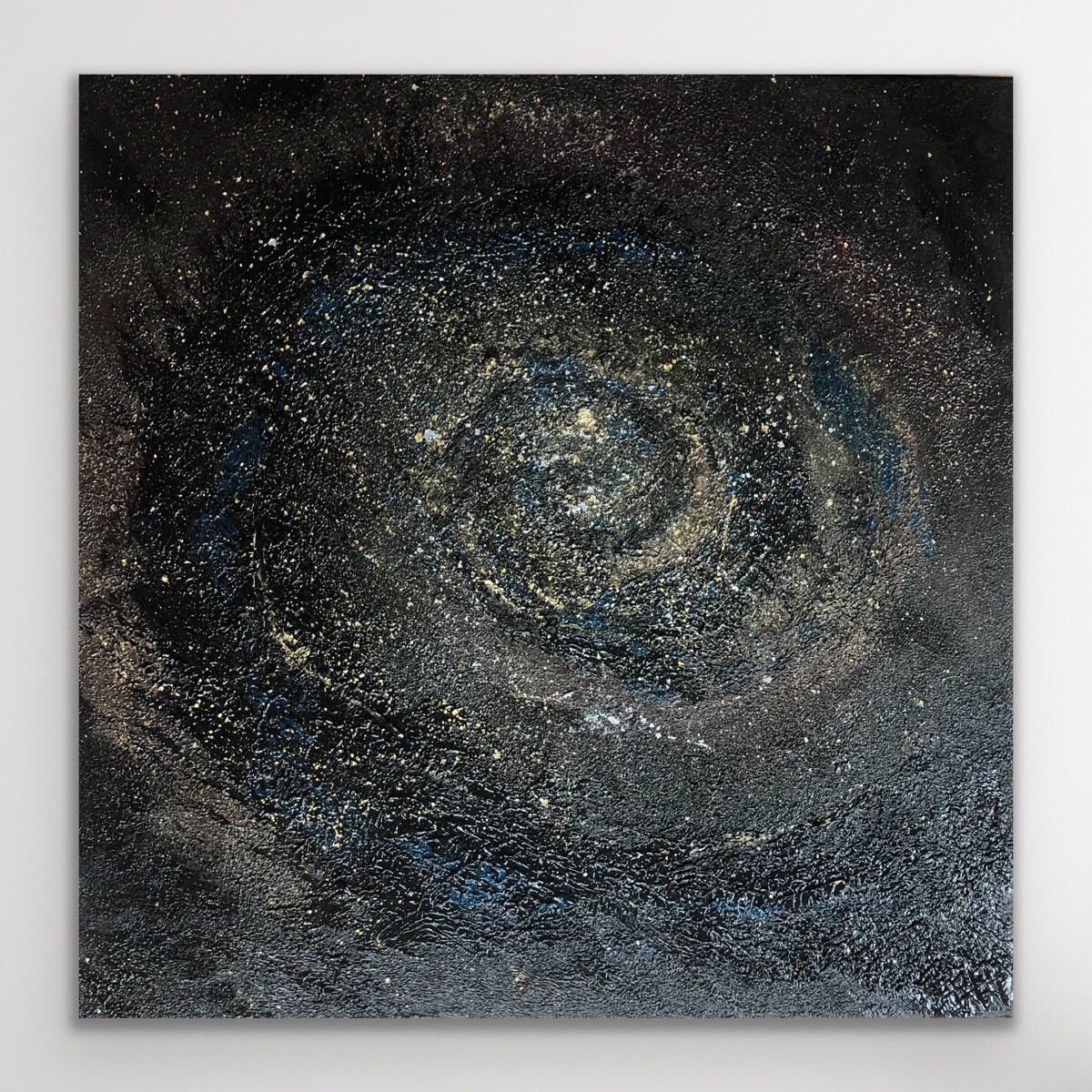 Abstrakcyjny obraz na płótnie w odcieniach czerni, złota i błękitu, przypominający spiralną galaktykę z wyraźną fakturą farby.