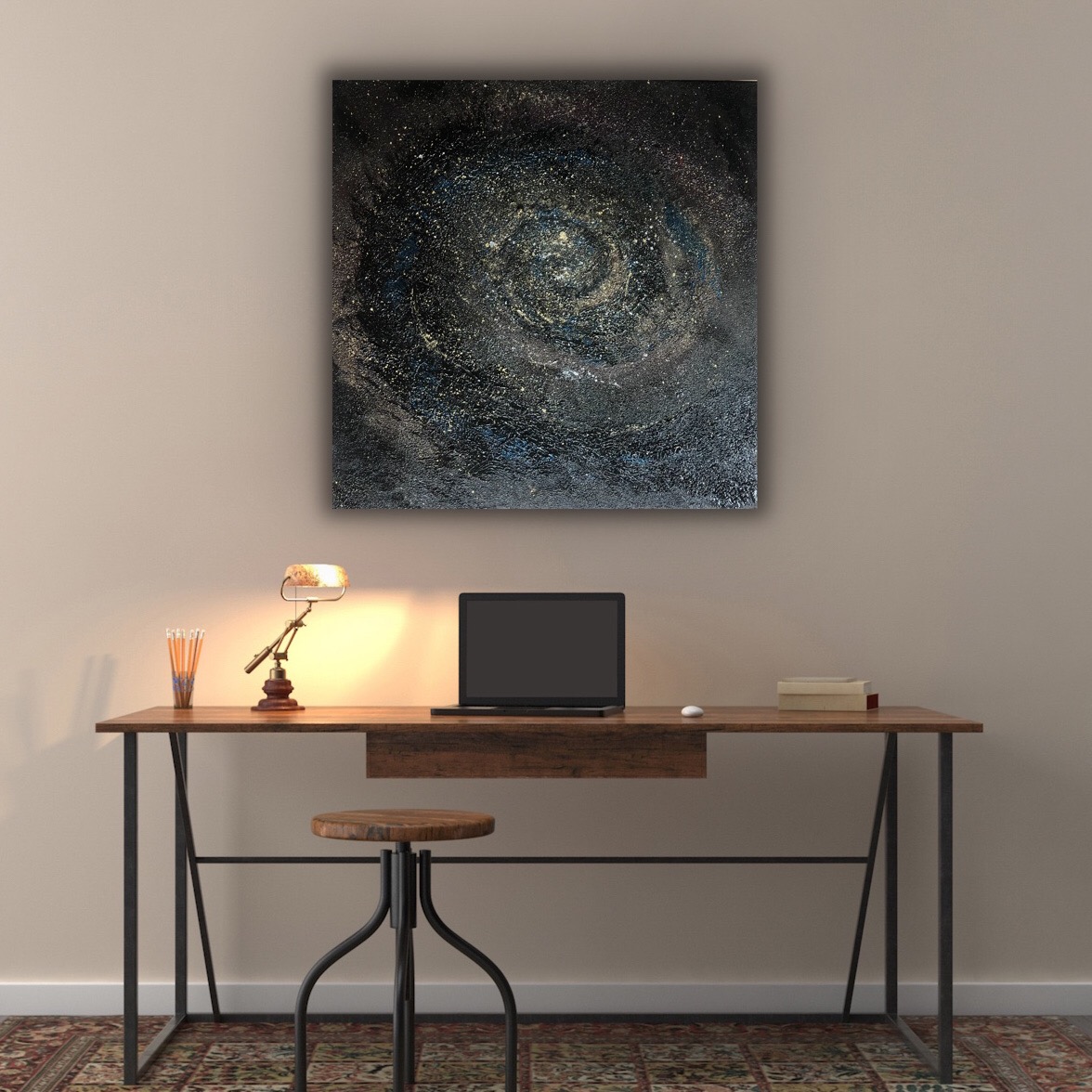 Abstrakcyjny obraz galaktyki z wirującymi złotymi i niebieskimi elementami, wiszący nad biurkiem z laptopem i lampką.