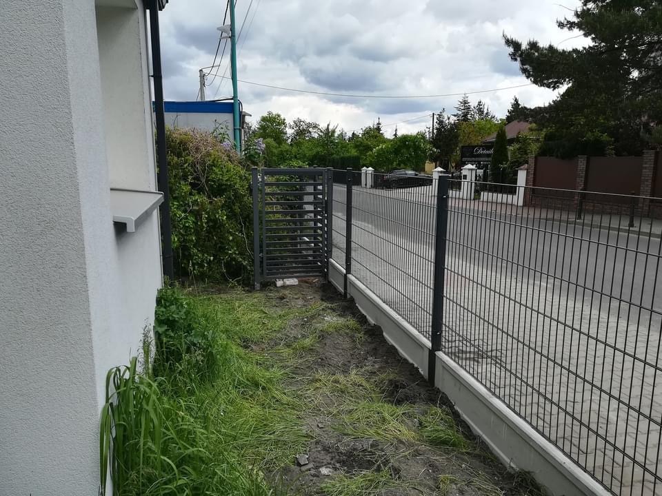 Nowoczesne ogrodzenie panelowe z bramką furtkową, betonowa podmurówka, widok z boku domu, zaniedbany trawnik.