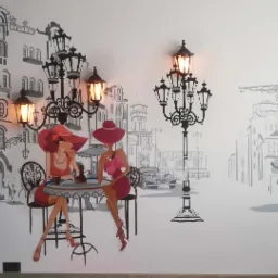 Artystyczne malowanie ściany przedstawiające dwie kobiety w kapeluszach siedzące przy stoliku w kawiarni w stylu retro, z elementami architektury miejskiej i latarniami ulicznymi w tle.