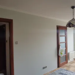Wnętrze pokoju w Jarosławiu po odświeżeniu ścian, z widocznymi gładkimi powierzchniami, wykończonymi listwami przysufitowymi i nowymi gniazdkami elektrycznymi.