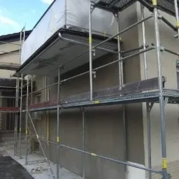 Elewacja domu w trakcie nakładania gładzi, widoczne rusztowanie z zabezpieczeniem przed warunkami atmosferycznymi.