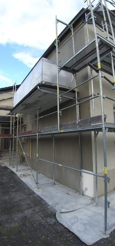 Elewacja domu w trakcie nakładania gładzi, widoczne rusztowanie z zabezpieczeniem przed warunkami atmosferycznymi.