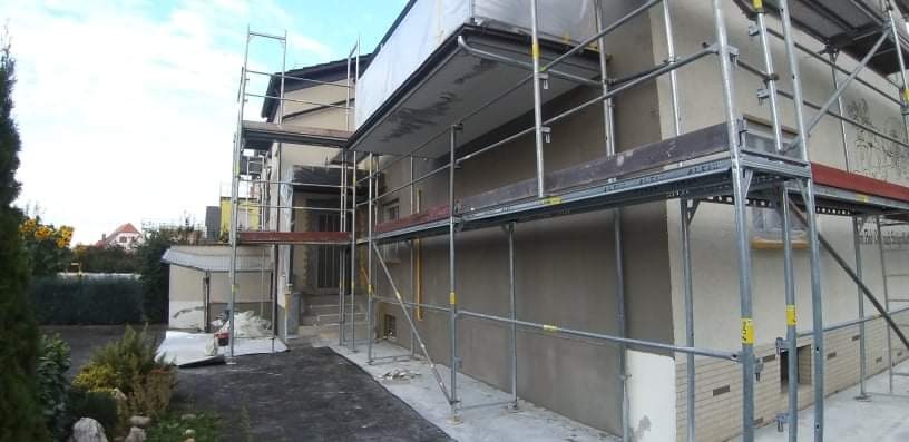 Dom w trakcie prac wykończeniowych elewacji, z widocznymi rusztowaniami i świeżo nałożoną warstwą tynku.