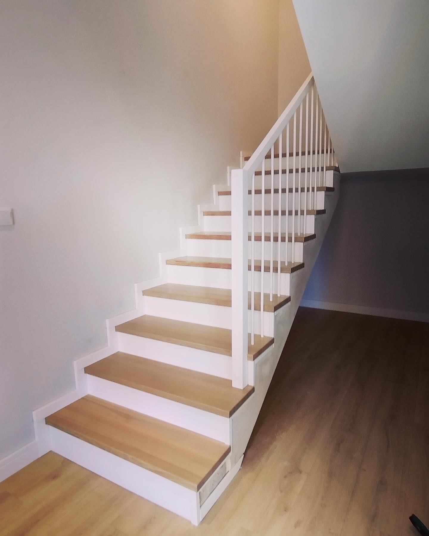 Nowoczesne, drewniane schody z białymi balustradami i podstopnicami, prowadzące na górę, widoczne z dołu, z parkietem na podłodze.