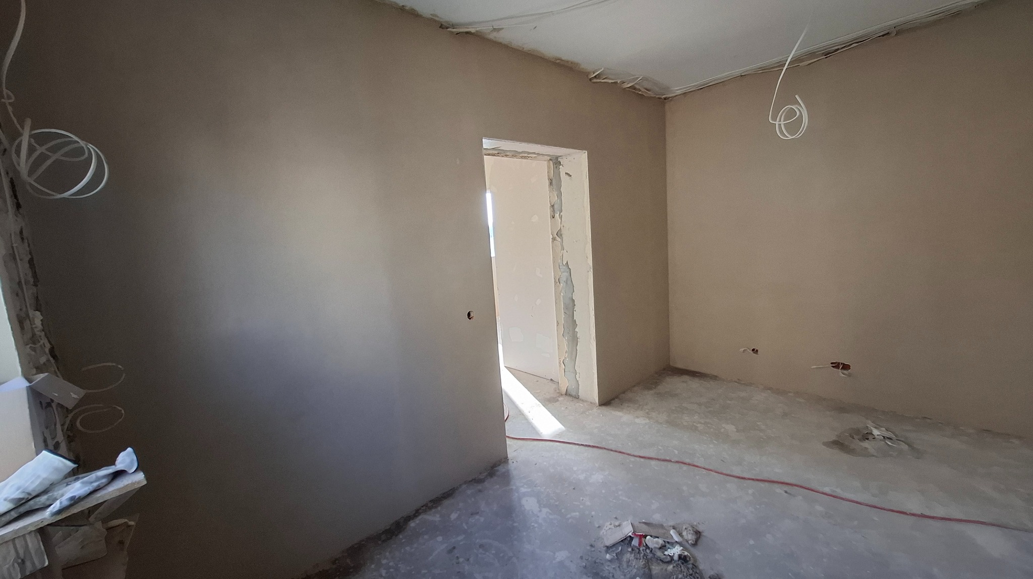 Pokój po szpachlowaniu ścian, widoczne gładkie powierzchnie i przygotowane otwory na instalacje elektryczne. Ościeżnica drzwiowa w trakcie obróbki.