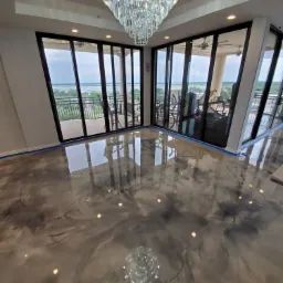 Błyszcząca, szara posadzka z efektem marmuru w przestronnym salonie z panoramicznymi oknami i kryształowym żyrandolem.