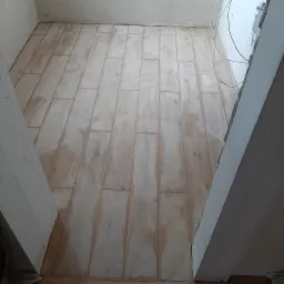 Ułożona, ale jeszcze zabrudzona, podłoga z płytek imitujących drewno w trakcie remontu. Widoczne surowe ściany i wystające kable.