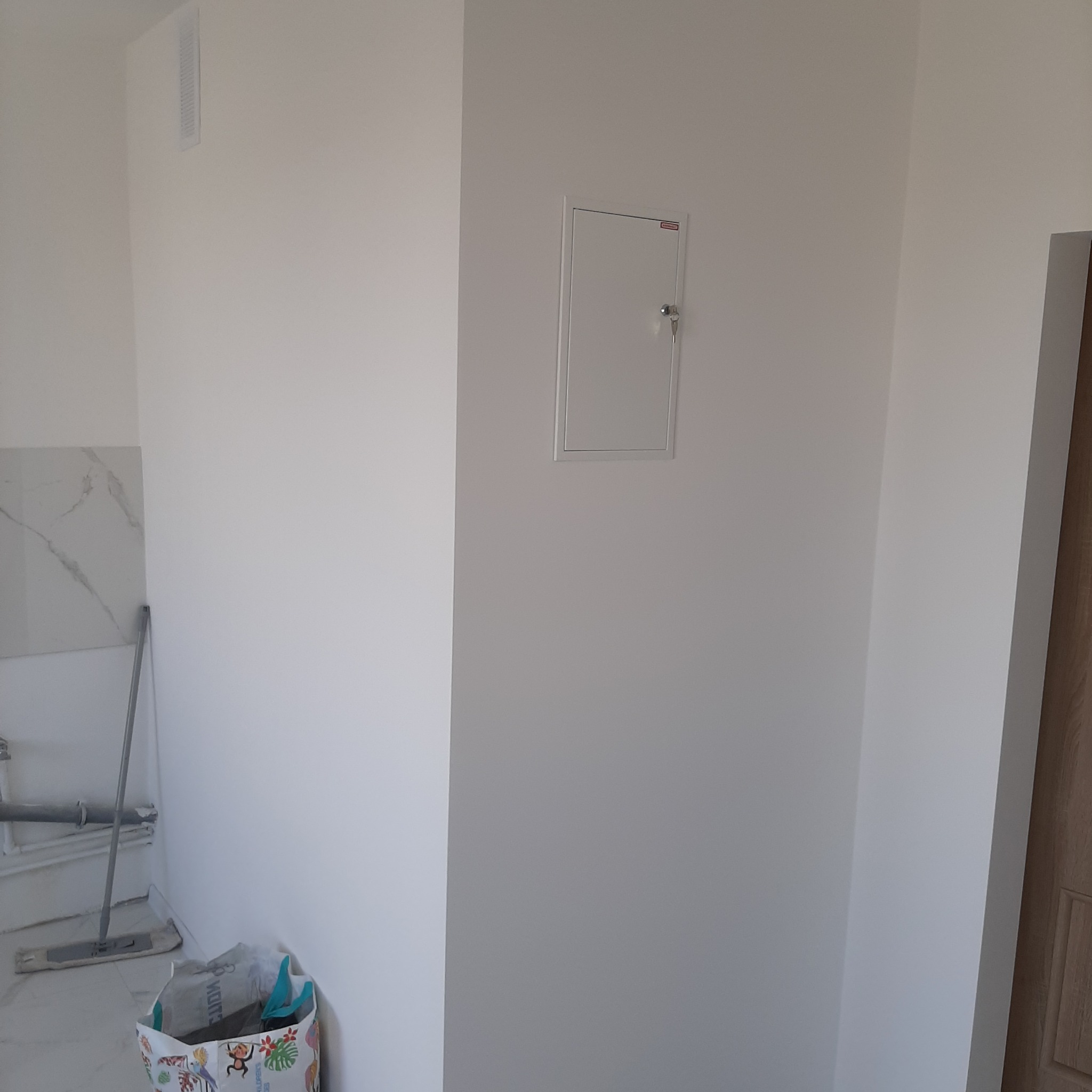 Świeżo pomalowane, białe ściany wewnętrzne z ukrytą szafką rewizyjną i fragmentem marmurowej ściany oraz mopem w rogu