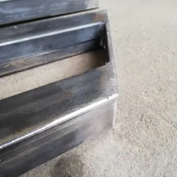 Metalowe profile prostokątne, przygotowane do spawania, leżące na szarej, betonowej powierzchni.