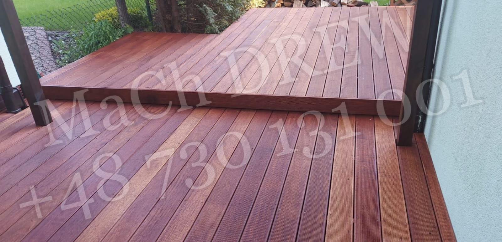 Brązowy taras z desek kompozytowych z dwoma poziomami, widoczne słupki zadaszenia i ściana budynku w tle.