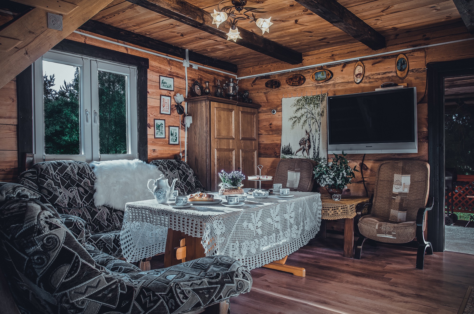 Wnętrze drewnianego domku letniskowego z nakrytym stołem, kanapą i telewizorem na ścianie.