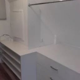 Biała szafa na wymiar z drążkiem na ubrania, półkami na buty i szufladami, dopasowana do skosu dachu.