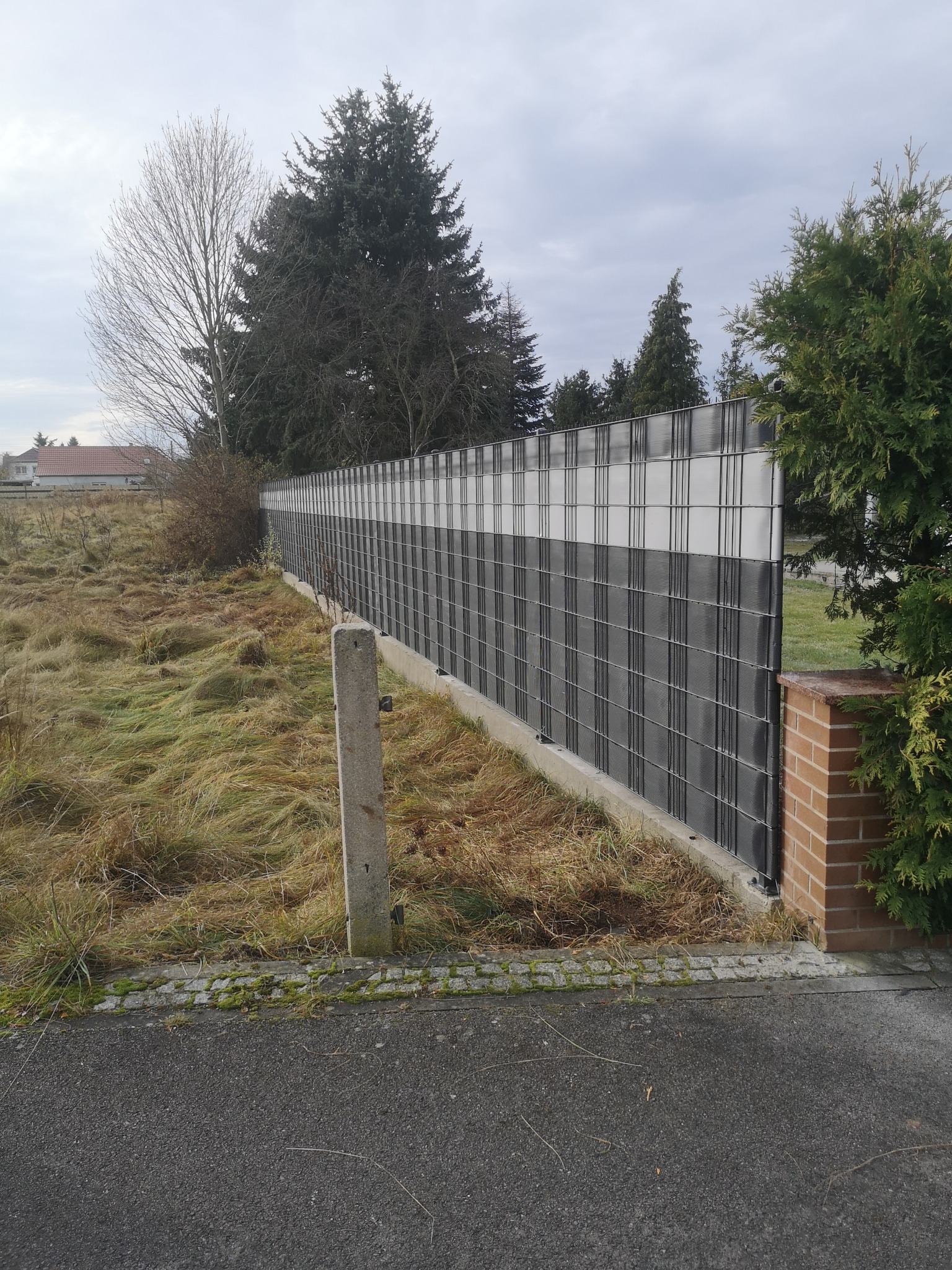 Nowoczesne ogrodzenie panelowe z podmurówką betonową i wypełnieniem z tworzywa sztucznego w kolorze szaro-białym, widoczne z perspektywy ulicy.