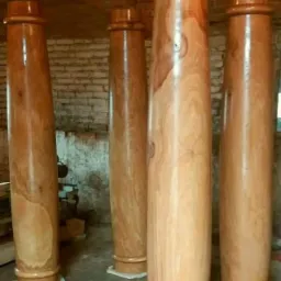 Polerowane drewniane kolumny o toczonych podstawach i zwieńczeniach, ustawione w pomieszczeniu z ceglaną ścianą w tle, prawdopodobnie przygotowane do montażu w altanie lub pergoli.