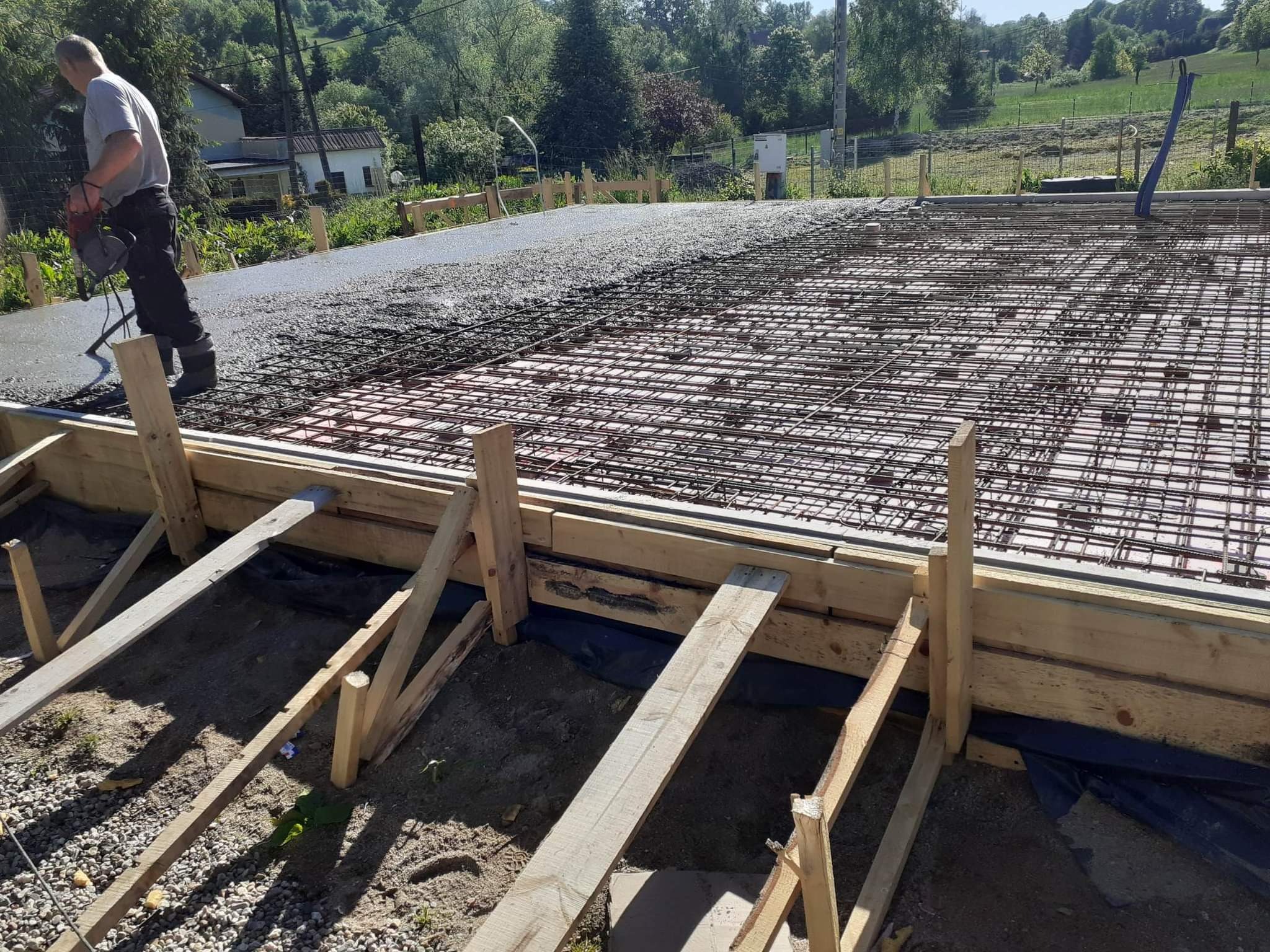 Wylewanie betonu na zbrojenie fundamentu domu jednorodzinnego, widoczny pracownik zacierający powierzchnię betonu i szalunek z desek.