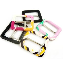 ALPINA Paulina Chyc - Zestaw pięciu kwadratowych sprzączek do paska, w tym jedna czarna skórzana, a pozostałe obszyte tkaninami w różne wzory i kolory: różowo-biały, żółto-brązowo-biały, różowo-zielono-biały...