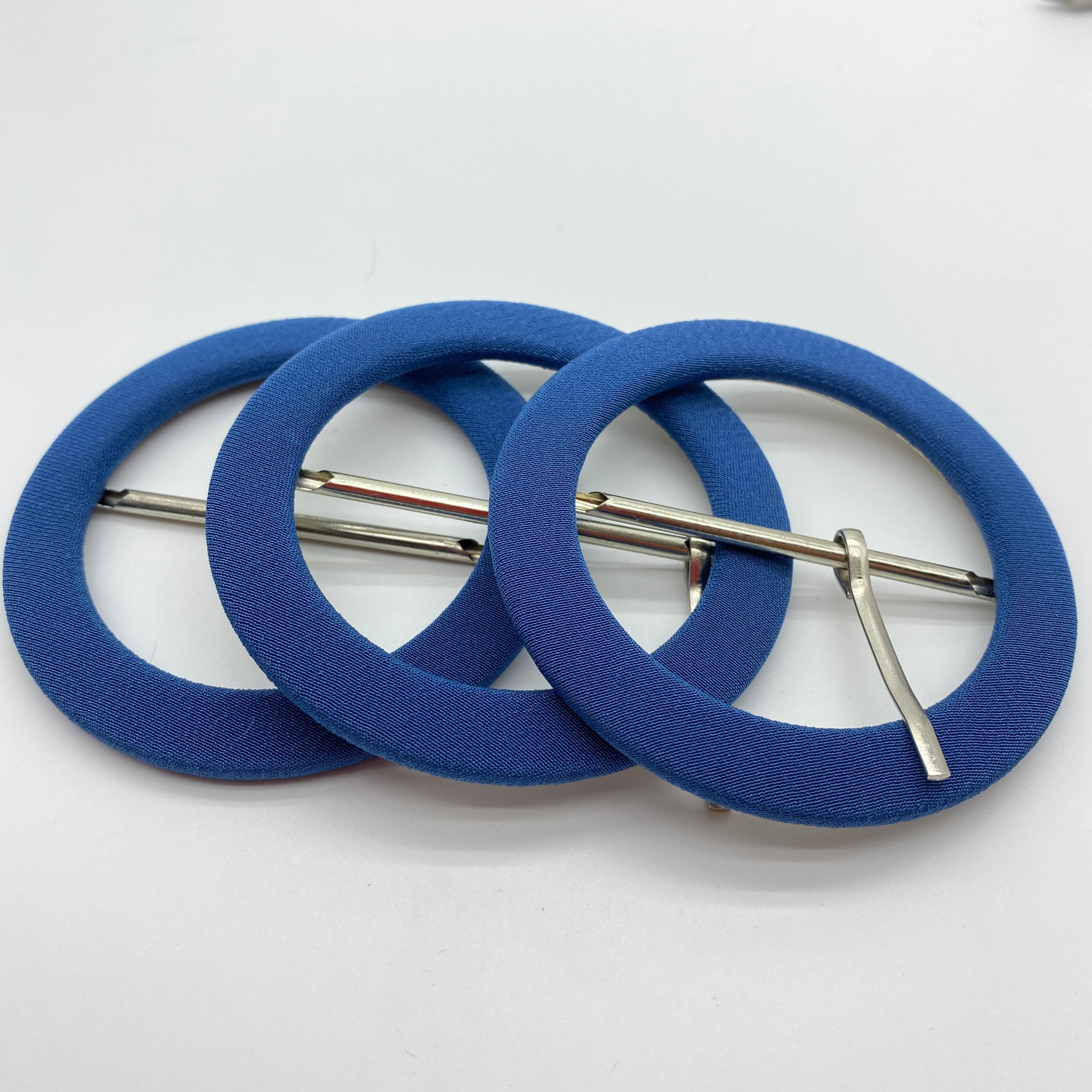 Trzy niebieskie, okrągłe elementy wykończeniowe z metalowymi zaczepami na białym tle, prawdopodobnie używane w produkcji odzieży.