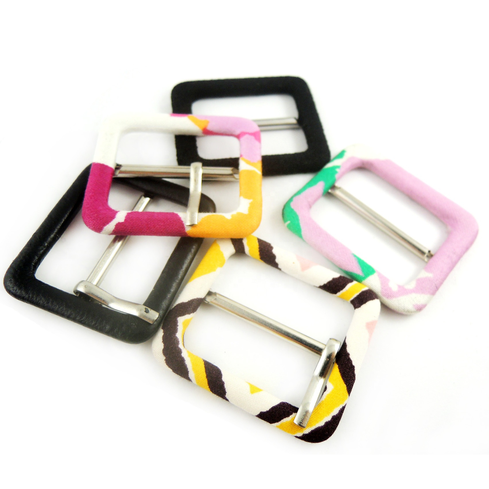 Zestaw pięciu kwadratowych sprzączek do paska, w tym jedna czarna skórzana, a pozostałe obszyte tkaninami w różne wzory i kolory: różowo-biały, żółto-brązowo-biały, różowo-zielono-biały...
