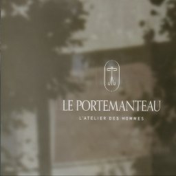 Momo Brand Studio - Eleganckie logo 'LE PORTEMANTEAU L'ATELIER DES HOMMES' na matowej szybie z delikatnym odbiciem otoczenia. Minimalistyczny design, stonowana kolorystyka i subtelny detal.