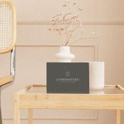 Momo Brand Studio - Eleganckie pudełko z logo 'Le Portemanteau' na szklanym stoliku, obok wazon z suszonymi kwiatami i krzesło w tle. Stonowana kolorystyka, minimalistyczny styl.