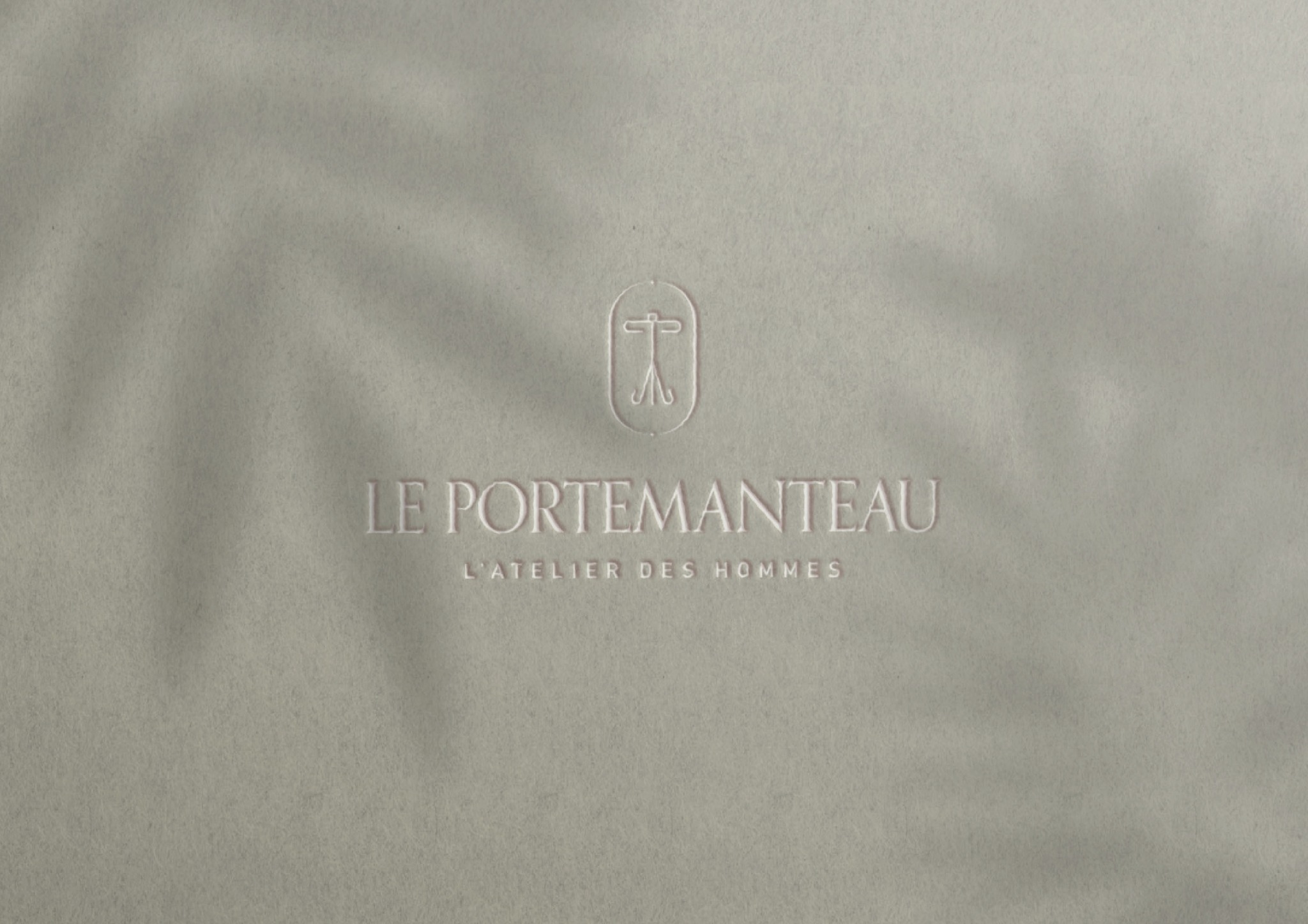 Eleganckie tłoczenie logo 'Le Portemanteau' na delikatnym papierze w Krakowie, z subtelnym cieniem liści. Minimalistyczny projekt identyfikacji wizualnej.