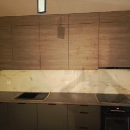 MEBLEGO SPÓŁKA Z OGRANICZONĄ ODPOWIEDZIALNOŚCIĄ - Nowoczesna kuchnia z górnymi szafkami w odcieniach drewna i szarymi dolnymi szafkami, marmurowy panel nad blatem, płyta indukcyjna i piekarnik elektryczny.