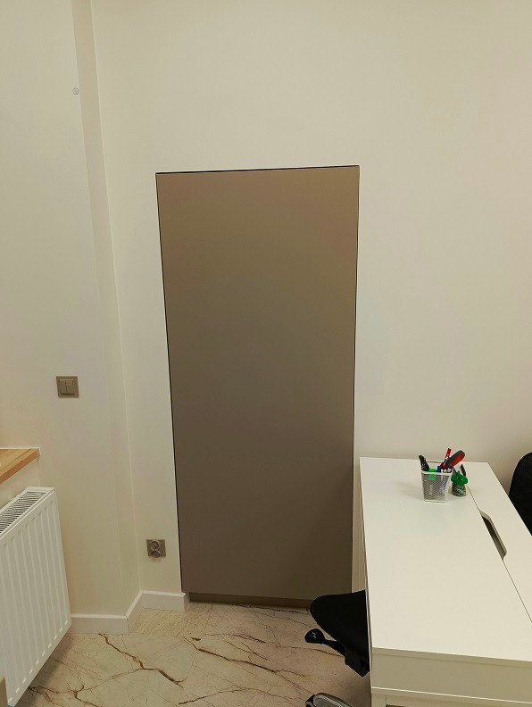 Beżowa szafa wnękowa zintegrowana ze ścianą, obok białe biurko z przyborami do pisania, marmurowa podłoga.