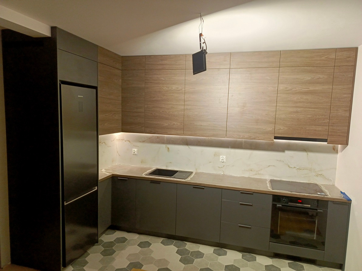 Nowoczesna kuchnia z szarymi szafkami dolnymi i drewnopodobnymi górnymi, marmurowy backsplash, heksagonalna podłoga, widoczny fragment wiszącej lampy.