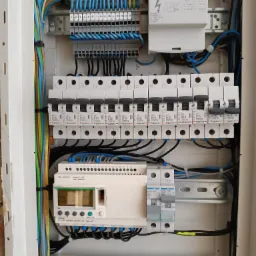 Rozdzielnica elektryczna z zamontowanymi bezpiecznikami, przewodami i programowalnym sterownikiem logicznym Schneider Electric Zelio Logic, widoczne oznaczenia B10 i B16 na wyłącznikach,  przewody...